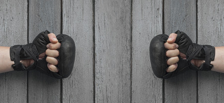 Two men hands in black leather gloves for Thai boxing clenched on gray worn wooden background, hands...