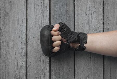 Hand man in black leather gloves for Thai boxing clenched on a gray shabby wooden backgroundの写真素材