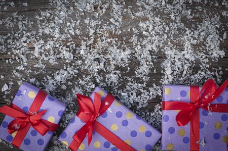 Three gift package with a red ribbon on a wooden surface with snow, empty space