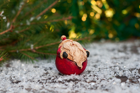 Ceramic Santa Claus on a small snow-covered wood surface, blurry background with lightsの写真素材