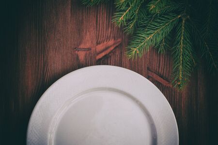 Half of an empty white plate on brown wooden surface, in the corner of a branch of spruce, vintage toningの写真素材