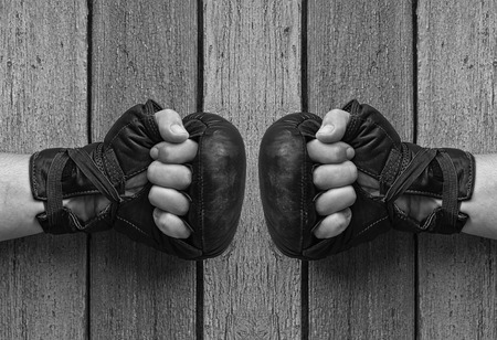 men hands in black leather gloves for Thai boxing clenched on gray worn wooden background, hands opposite each other, black and white toningの写真素材