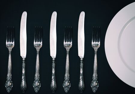 Half empty white plates, vintage knife and fork on black table, view from above の写真素材