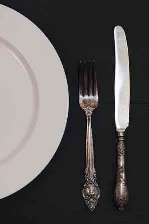 Half empty white plates, vintage knife and fork on black table, view from above の写真素材
