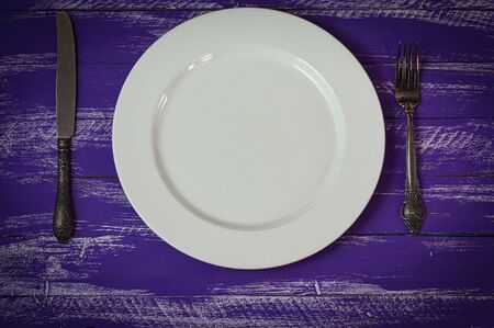 white plate with cutlery on a lilac wooden surface, the view from the topの写真素材