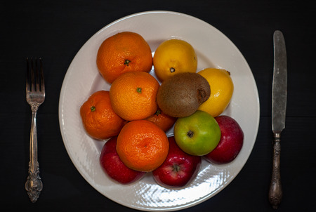 Ripe fruit on a white plate, black table, top viewの写真素材
