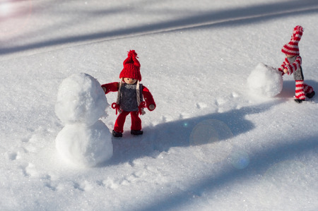 building a snowman made of snow scene with two small wooden dolls smiling faces in winter red clothesの写真素材