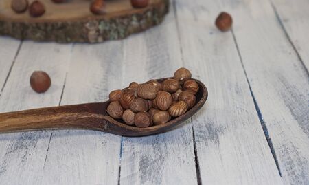 Peeled hazelnuts from the shell in a wooden spoon on a white wooden surfaceの写真素材