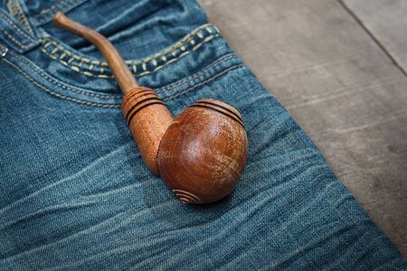 Smoking wooden pipe on blue jeans