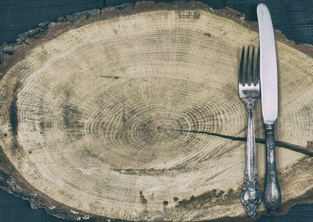 Fork and knife on a brown wooden stump, empty space, vintage toningの写真素材