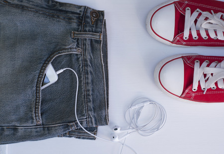 Blue jeans with mobile phone in the pocket near Youth red shoes, top viewの写真素材