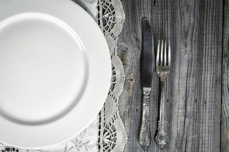 White empty plate on the tablecloth with lace, near knife and fork, top viewの写真素材