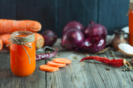 Carrot fresh juice in a glass container among the vegetables and spices on gray wooden surface, selective focusの写真素材