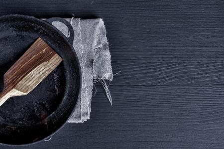 Frying pan with wooden spatula on a black surface, empty spaceの写真素材