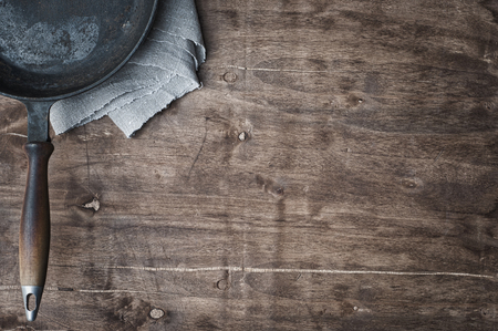 black frying pan on a brown wooden table, empty spaceの写真素材