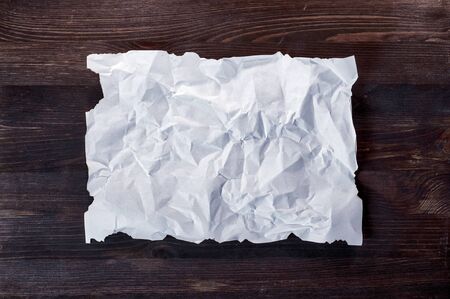 Crumpled white blank sheet with burnt edges on a brown wooden boardの写真素材