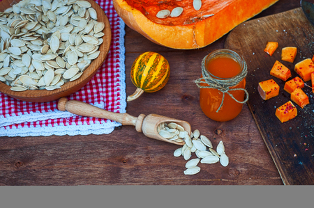 Pumpkin seeds and a piece of fresh pumpkin on a brown wooden surface, in a jar of pumpkin juiceの写真素材