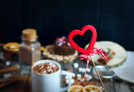 figure of a wooden heart on a stick on a background of cups with drink chocolate and sweets, vintage toningの写真素材
