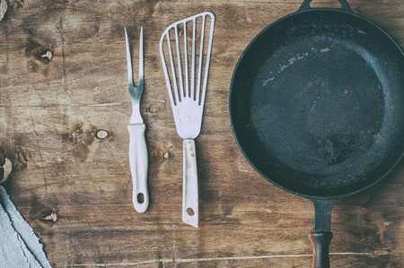 Empty black cast-iron frying pan with vintage kitchen items on a brown table, top view, vintage toningの写真素材