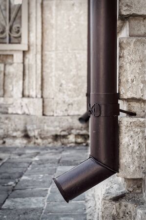 Brown metal drainpipe on the corner of a stone house