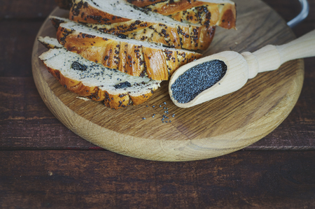 Bun with poppy on a cutting board and poppy in a wooden spoonの写真素材