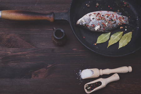 Fresh crucian in a frying pan with pepper and salt in a black frying pan, top view, vintage toning