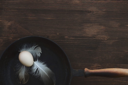 Raw chicken egg in a black cast-iron frying pan on a brown wooden surface, an empty space at the topの写真素材