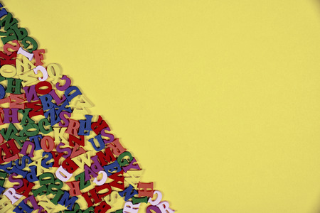 Multicolored wooden letters in the lower left corner on the yellow surface, empty spaceの写真素材
