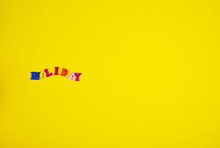 Inscription holiday of small wooden letters on a yellow surface, on the right an empty spaceの写真素材