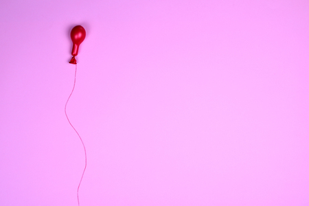 Red air balloon on a red string, pink background, blank space on the rightの写真素材