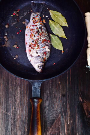 Fish carp in spices on a black cast-iron frying pan with a wooden handle, top view, vintage toningの写真素材