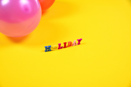 Inscription holiday of small wooden letters on a yellow surface, empty space on the rightの写真素材