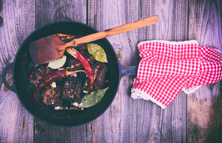 Cooked pork ribs on a black cast-iron frying pan with a handle, meat in spices and red chili pepper, top view, vintage toningの写真素材