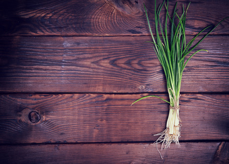 bunch of green onions on a brown wooden surface, an empty space on the leftの写真素材