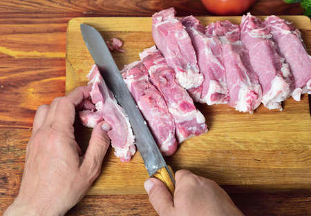Fresh pork meat on the kitchen board, men's hands cut into pieces, vintage toningの写真素材