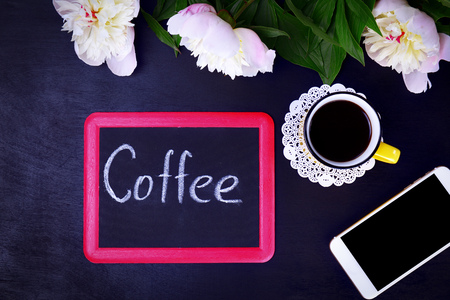 Black chalkboard with an inscription of coffee, next to a smartphone and a yellow cup with coffee, top viewの写真素材