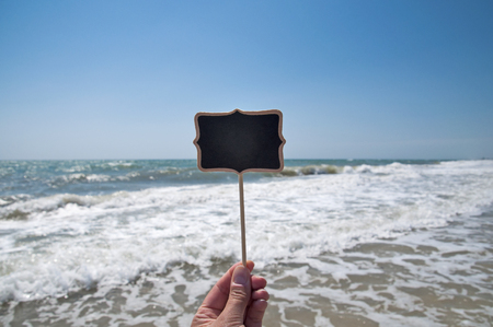 Empty wooden plaque in hand against the background of the sea, summer dayの写真素材
