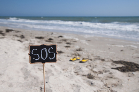 Wooden plaque with an inscription SOS on the background of the sea and sandy beachの写真素材