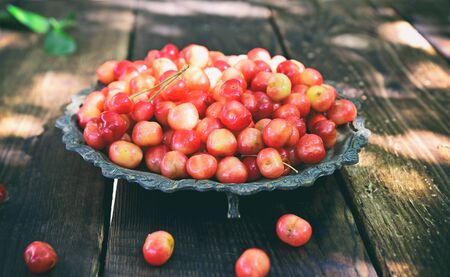 Pink cherry in a metal plate on a wooden table, vintage toningの写真素材