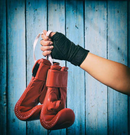 Female hand holds a pair of red kickboxing gloves on a blue wooden backgroundの写真素材