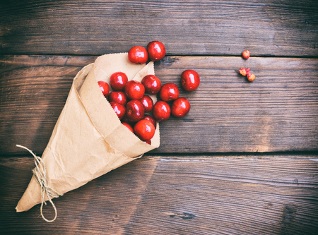Ripe red cherry in a paper bag on a brown wooden background, empty space on the rightの写真素材