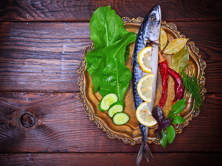 Mackerel with spices and herbs on a copper plate, brown wooden background, empty space on the leftの写真素材