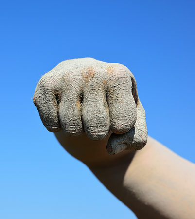 Male fist smeared with mud on blue sky backgroundの写真素材