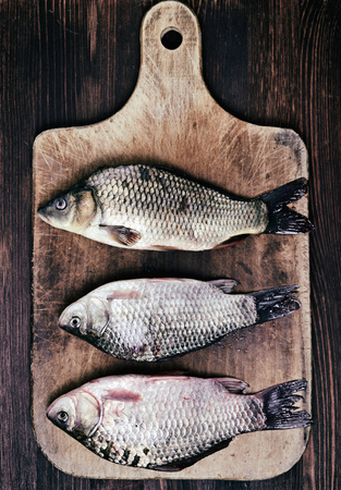 Three fresh river fish carp lie on a wooden kitchen cutting boardの写真素材