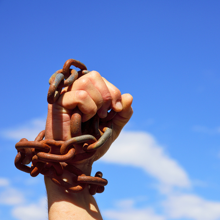 Man's hand is chained in iron chains against the skyの写真素材