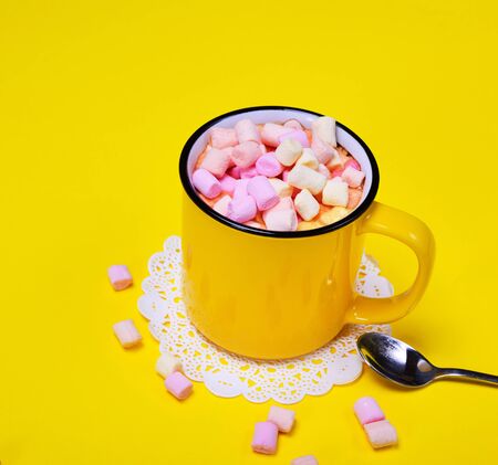 yellow mug with a cocoa drink and pieces of a multicolored marshmallow on a yellow backgroundの写真素材