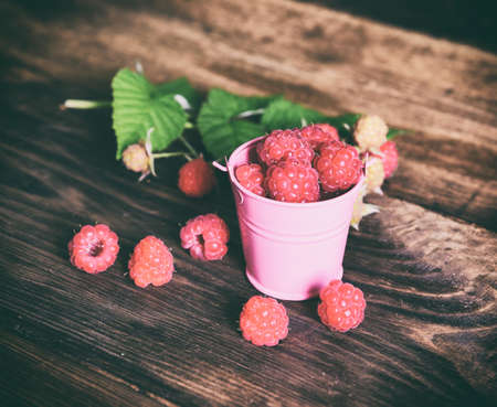 Ripe red raspberries in an iron bucket on a brown wooden background, vintage toningの写真素材