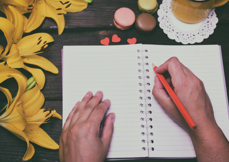 Open white paper notebook and two hands of a man with a red pencil, top viewの写真素材