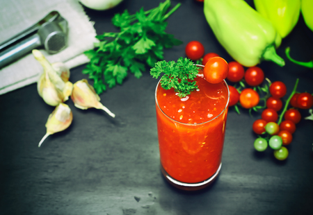 Freshly made juice from a tomato and spices in a glass on a black background, top view, behind fresh vegetablesの写真素材