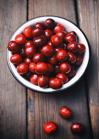 Ripe red cherry in an iron bowl on a brown wooden backgroundの写真素材